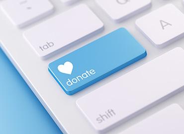 A white keyboard in which the caps lock key has been replaced with a blue button with the word "Donate" and a heart in white on it.